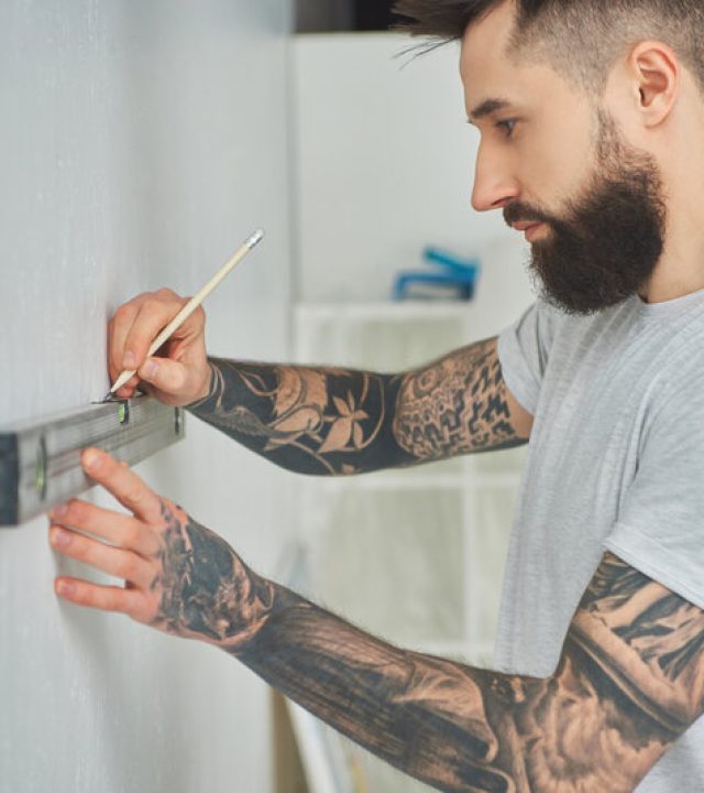 side view of handsome bearded young man holding level tool and pencil during home improvement
